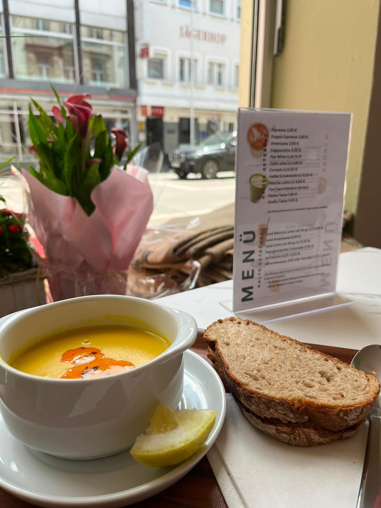 Hausgemachte Linsensuppe mit Zitrone und Brot am Fenster, daneben Tulpen und die Speisekarte