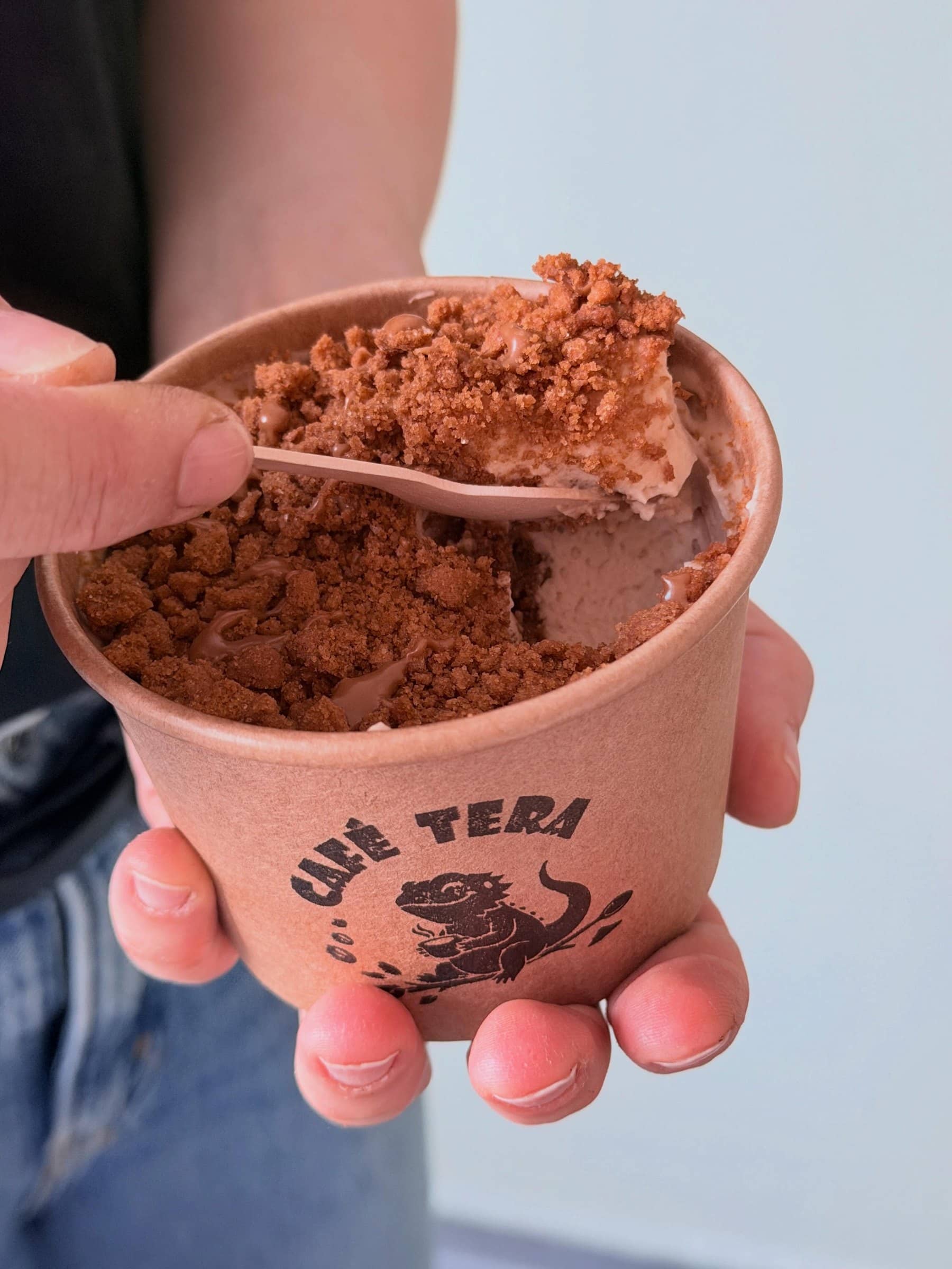 Ein Holzlöffel hebt cremiges Lotus-Tiramisu mit Biscoff-Streuseln aus dem Café-Tera-Becher